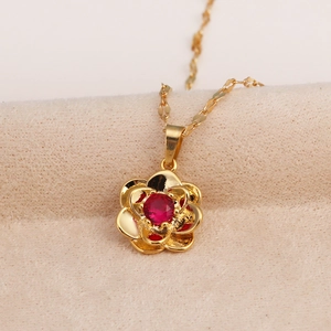 Detail of a gold rose pendant necklace with a red gemstone on a beige velvet surface