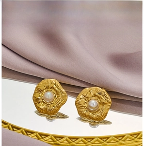 Macro view of gold flower earrings with white pearl centers on a vintage mirror