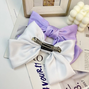 Detail view of large satin bow hair clips in purple and white with metal spring clips