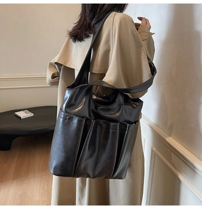 Black large capacity faux leather shoulder bag with multiple pockets worn over a beige coat