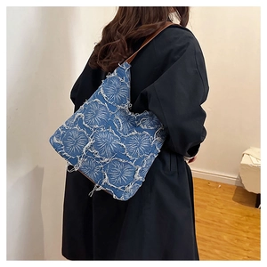 Close-up of blue denim shoulder bag with white geometric patterns and frayed edges on model
