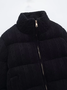 Detail of black cable knit puffer jacket featuring premium golden zipper and stand collar