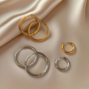 Polished gold and silver hoop earrings in multiple sizes on elegant beige silk fabric