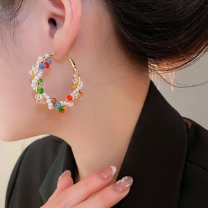 Detail of colorful crystal and pearl beaded hoop earrings worn by a model in a close-up shot