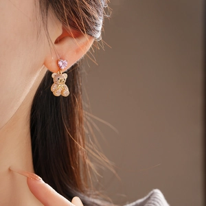 Détail d'une boucle d'oreille ours doré avec zircon cœur rose portée par un mannequin