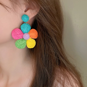Close-up of a model wearing colorful woven flower earrings with a bohemian summer vibe