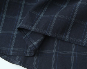 Detail of navy blue plaid cotton fabric showing precision stitching on shirt hemline