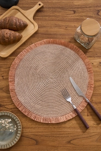 Detailed top view of rose gold woven placemat with tassels on dark wooden table