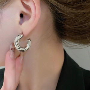 Detail shot of silver C-shaped hoop earrings with twisted texture worn by a model