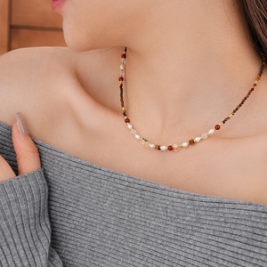 Tiger eye and pearl beaded necklace worn on neck over grey knitwear detail