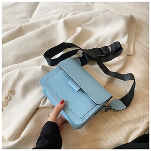 Detail of light blue crossbody bag with thick black nylon strap on white fabric