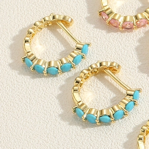 Détail de boucles d'oreilles huggies dorées avec zircons ovales roses et turquoise