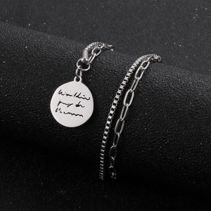 Silver double-layered chain bracelet with an engraved round pendant on a black surface