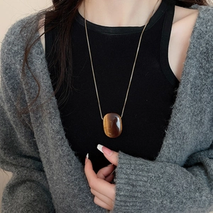 Close-up of a long golden necklace featuring a glossy amber resin oval pendant on a model