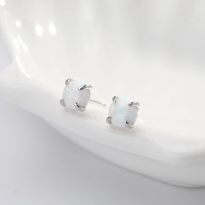 Macro view of white round opal stud earrings with silver four-prong setting