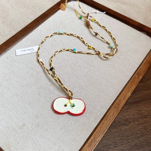 Handwoven necklace with colorful beads and a red apple pendant on a rustic display tray