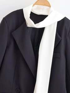 Detail of a black blazer featuring a contrasting white scarf on a wooden hanger