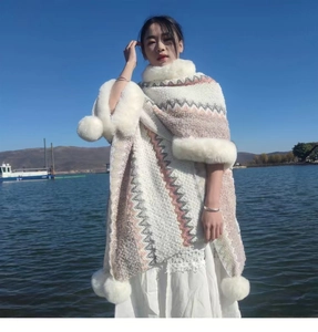 Close-up of knit shawl with faux fur collar and pompom details on a lakeside