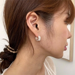 Detail of silver C-shape pearl hoop earring with bead-edge finish worn by a model