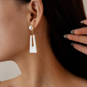 Close-up of elegant gold drop earrings with white pearl and shell-textured trapezoid pendant