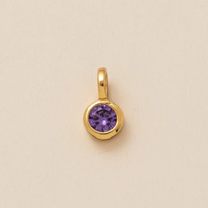 Macro view of a circular purple zircon pendant with a polished gold bezel setting