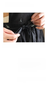 Detail of black cotton apron waist showing elegant white leaf embroidery and pleated design