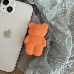 Close-up of a matte orange 3D bear pop socket grip attached to a clear phone case