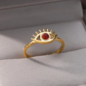 Macro detail of golden twist ring featuring a red bead evil eye design in a jewelry box