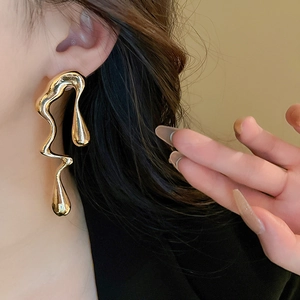 Detail of irregular liquid metal gold drop earring worn by a model in a high-fashion style