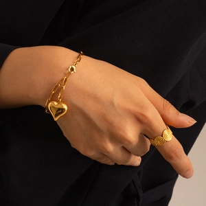 Detailed view of a gold paperclip chain bracelet with a heart pendant and textured ring