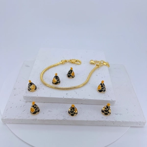 Detail of gold snake chain bracelet with black and gold conical charms on stone base