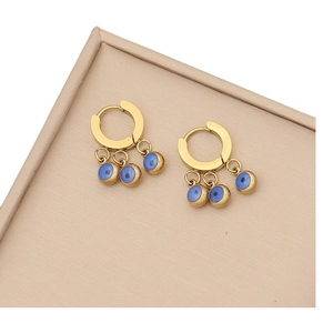 Golden stud earrings with triple blue evil eye charms on a beige jewelry display tray