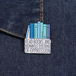 Close-up of enamel pin with slogan on denim jacket showing stacked books and blue tones