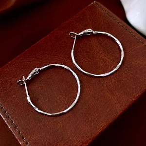 Macro shot of silver hammer-textured hoop earrings on dark brown leather texture