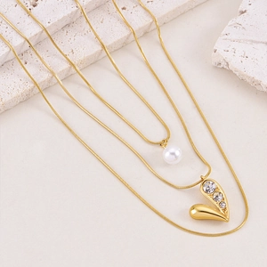 Close-up of layered gold snake chain necklace with pearl and sparkling heart pendant