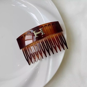 Macro detail of tortoiseshell hair comb with golden H logo on white ceramic plate