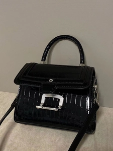Detailed view of black crocodile pattern leather handbag with silver metal buckle