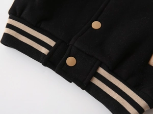 Detail of boys' varsity jacket showing black fabric, ribbed hem and round snap buttons