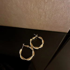 Vista detallada de aretes de aro dorados retorcidos con textura metálica elegante