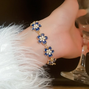 Close-up of a floral enamel bracelet in blue and white on a model wrist with fur cuff