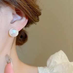 Close-up of elegant large mermaid pearl stud earrings worn by a model in warm light
