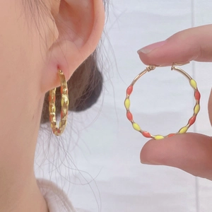 Boucles d'oreilles créoles dorées avec émail géométrique coloré portées par mannequin