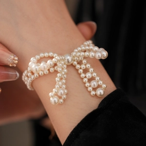 Elegantes weißes Perlenarmband mit Schleife, getragen von einem Model auf dunklem Grund