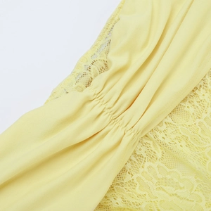 Detail view of light yellow lace stitching and pleated fabric texture on the dress