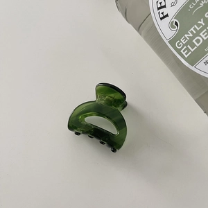 Detailed top view of a dark green acetate hair claw clip on a white minimalist background