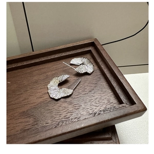 Macro detail of silver fan-shaped pleated earrings on a dark brown wood tray