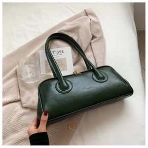 Close-up of a dark green cylindrical shoulder bag with gold zipper on beige corduroy