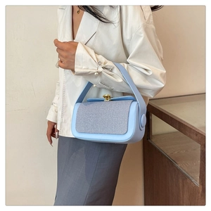 Close-up of a light blue contrast handbag with metal buckle worn by a model in white top