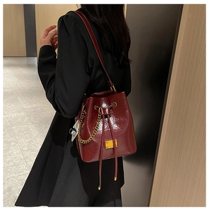 Détail du sac seau en cuir rouge foncé avec chaîne dorée et breloque boule 8 tendance