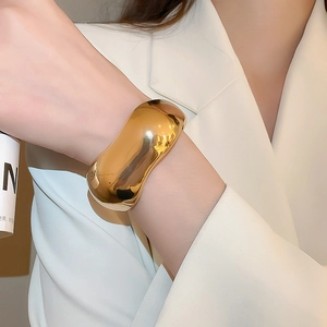 Close-up of polished gold wavy wide cuff bracelet styled with a minimalist white blazer